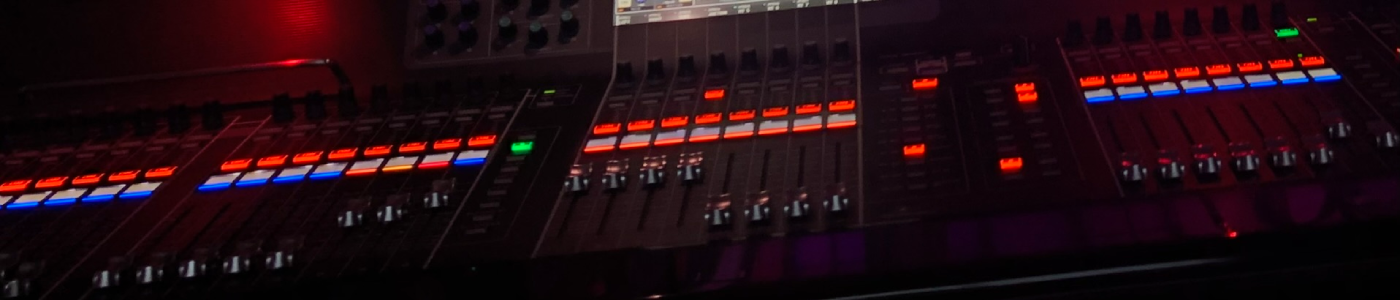 Close-up of a professional LED lighting console showing multiple motorized faders with illuminated red and blue status buttons, encased in a glossy black panel under low ambient light