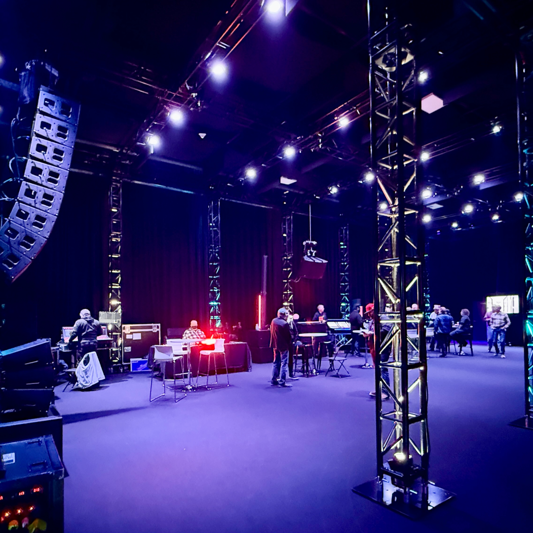 Professional virtual studio setup in a black-draped production space featuring a curved LED video wall branded ‘LEGACY Production Group’, two high-definition broadcast cameras on tripods with attached monitors and cables, and surrounding studio lighting, ready for live streaming or virtual event production