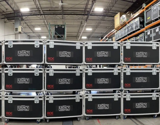 Two black Martin MAC Aura XB moving-head LED wash fixtures with multi-lens front panels, mounted side by side on black risers against a gray fabric backdrop, ready for vibrant color washes in event stage lighting setups